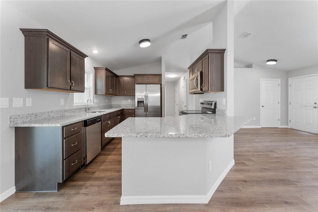 A kitchen features dark wood cabinets, granite countertops, stainless steel appliances, and wood-look flooring — 9461 N SANDREE DRIVE, CITRUS SPRINGS, FL