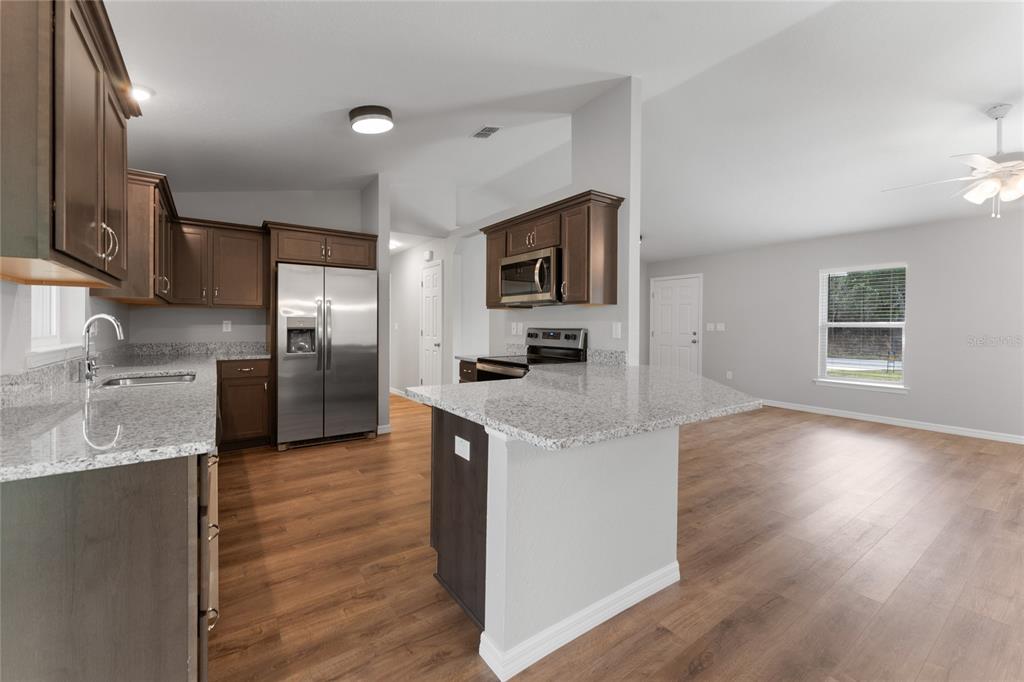 A kitchen with dark wood cabinets, granite countertops, and stainless steel appliances opens to a living area — 9461 N SANDREE DRIVE, CITRUS SPRINGS, FL