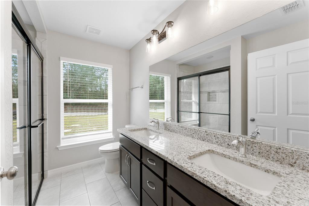 A bathroom features a double vanity with granite countertops, dark cabinets, and a glass-enclosed shower — 9461 N SANDREE DRIVE, CITRUS SPRINGS, FL