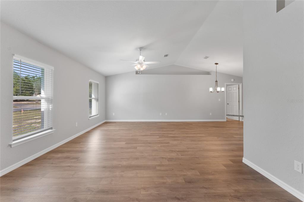 An empty living room features light gray walls, wood-look flooring, a vaulted ceiling, and windows — 9461 N SANDREE DRIVE, CITRUS SPRINGS, FL