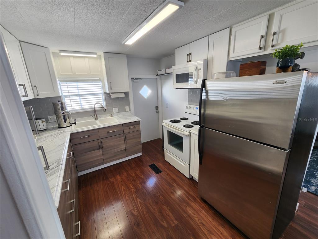 A kitchen features white upper cabinets, wood-tone lower cabinets, stainless steel appliances, and wood flooring — 2204 17TH STREET COURT W, BRADENTON, FL