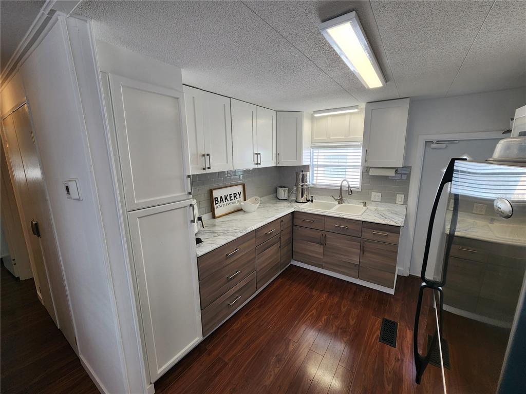 A kitchen features white upper cabinets, wood-tone lower cabinets, marble-look countertops, and dark wood flooring — 2204 17TH STREET COURT W, BRADENTON, FL