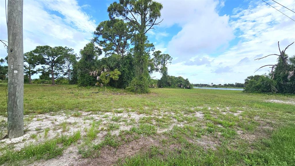 A grassy, undeveloped lot features scattered trees and shrubs with a view of water — 56 BRIG CIRCLE E, PLACIDA, FL