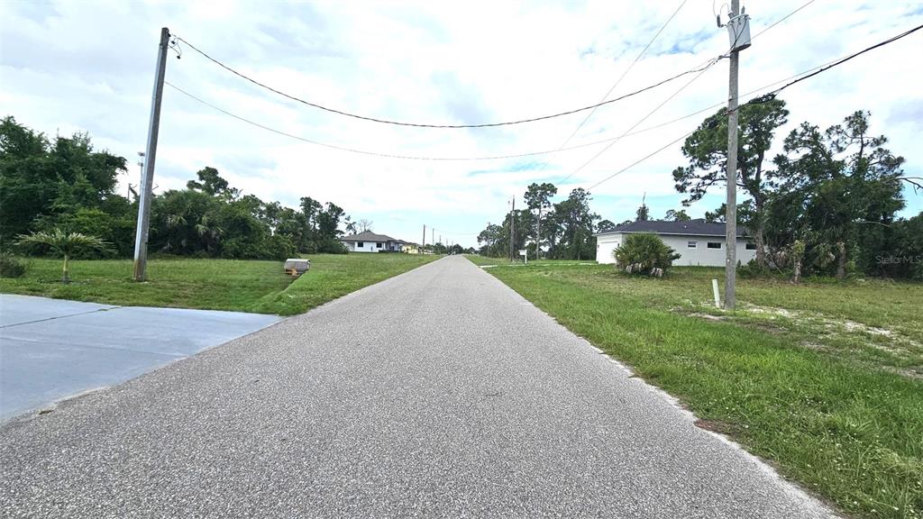A paved road stretches between grassy lots with trees and houses under a cloudy sky — 56 BRIG CIRCLE E, PLACIDA, FL