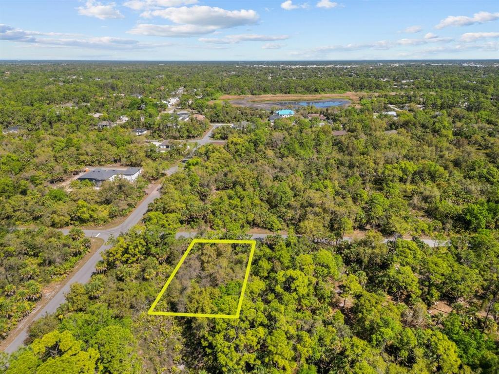 An aerial view shows a vacant, wooded rectangular lot outlined in yellow near a paved road — 18047 SAVAGE AVENUE, PORT CHARLOTTE, FL