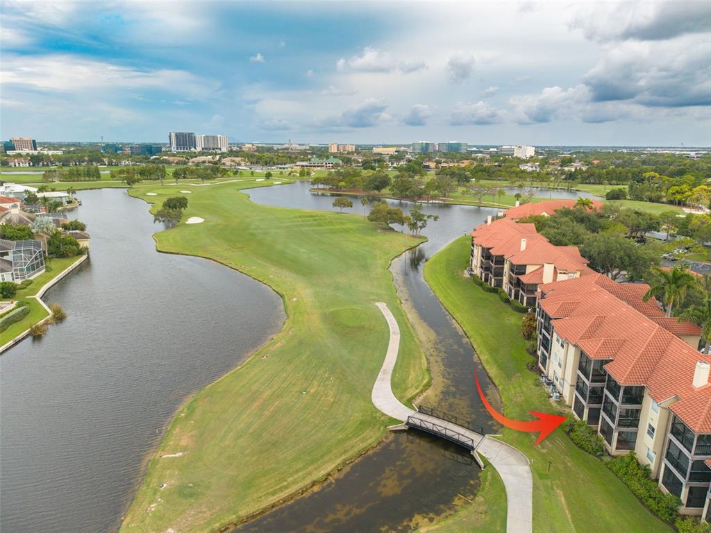 An aerial view shows a multi-story apartment building beside a golf course and a lake — 2400 FEATHER SOUND DRIVE UNIT 914, CLEARWATER, FL