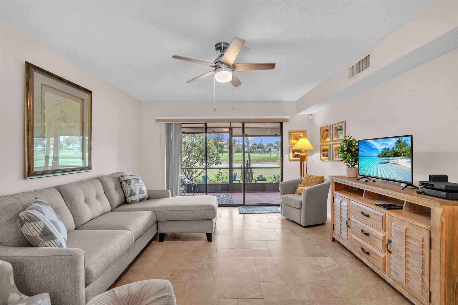 A living room features a gray sectional sofa, a wooden media console, and sliding glass doors — 2061 Keystone Drive # B, Jupiter FL 33458, JUPITER, FL