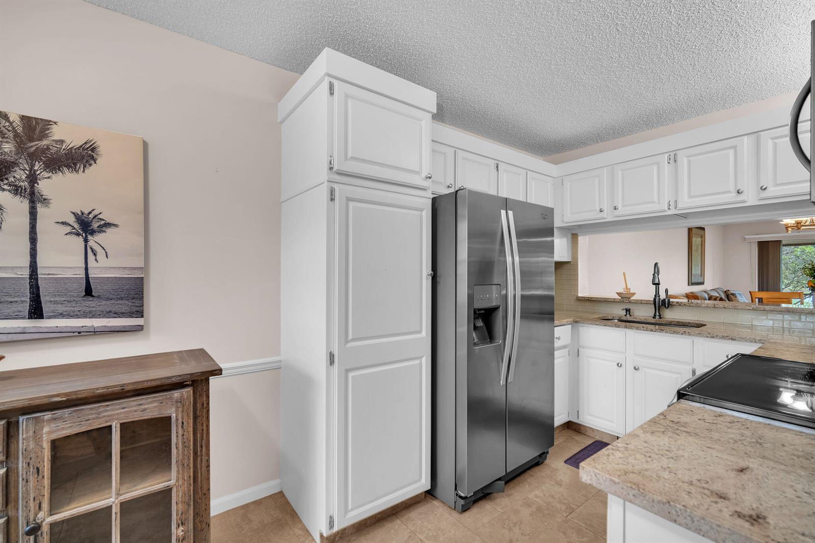 A kitchen features white cabinetry, a stainless steel refrigerator, and beige granite countertops — 2061 Keystone Drive # B, Jupiter FL 33458, JUPITER, FL