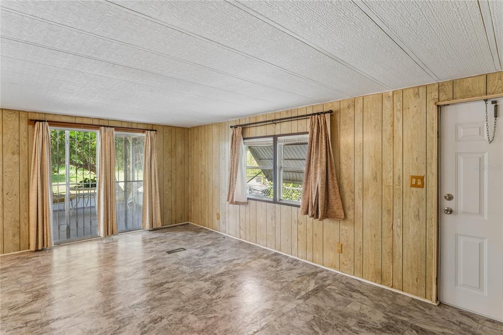 A room with wood-paneled walls, marble-patterned flooring, a sliding glass door, and a white door — 6601 SUTHERLAND AVE, NEW PORT RICHEY, FL