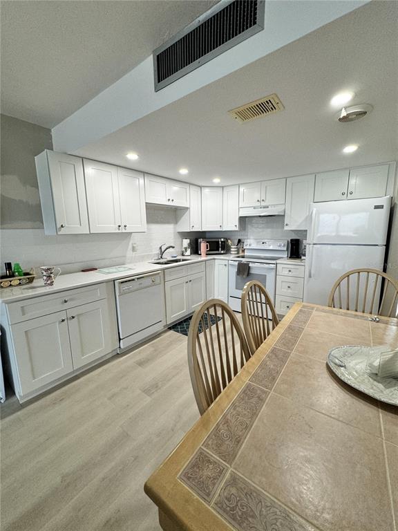 A kitchen features white cabinets, light countertops, stainless steel appliances, and a tiled dining table — 4849 SAXON DRIVE UNIT A208, NEW SMYRNA BEACH, FL