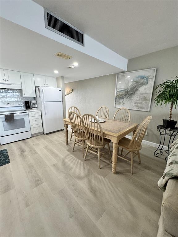 A kitchen and dining area feature light wood-look flooring, white cabinetry, and a wooden table — 4849 SAXON DRIVE UNIT A208, NEW SMYRNA BEACH, FL