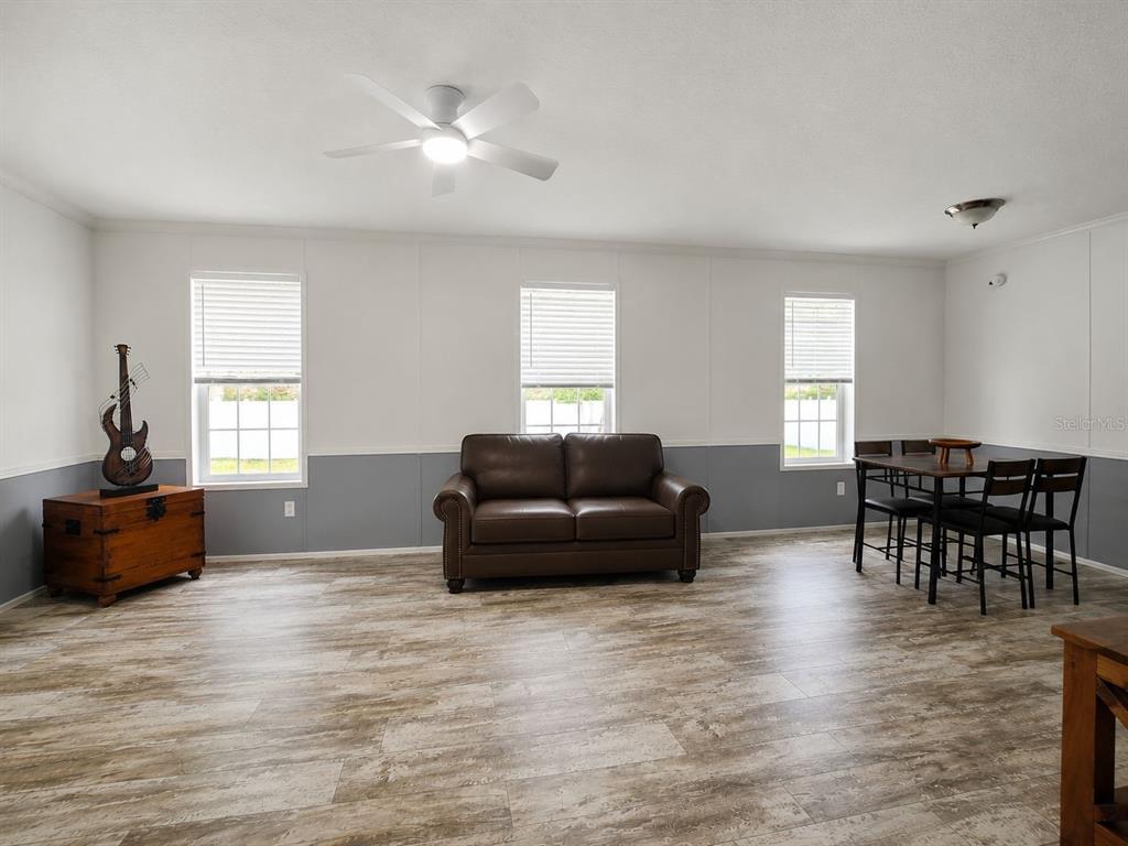 A grassy backyard features a white vinyl privacy fence and mature trees under a blue sky — 55515 LISA STREET, ASTOR, FL