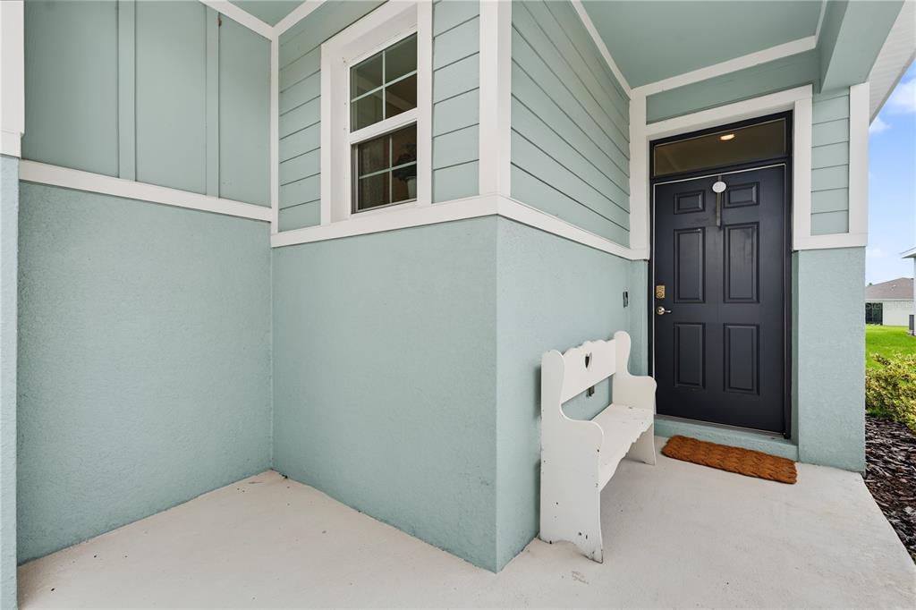A light blue exterior entryway features a dark front door, a white bench, and a window — 5285 SUNSHINE DRIVE, WILDWOOD, FL