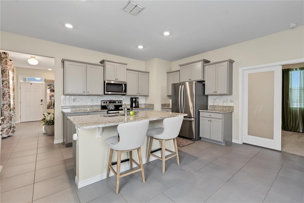 A kitchen features gray cabinets, granite countertops, a central island with bar stools, and tile flooring — 5285 SUNSHINE DRIVE, WILDWOOD, FL