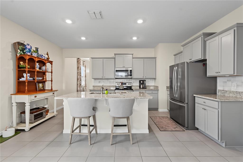 A kitchen features gray cabinets, granite countertops, a central island with two stools, and tile flooring — 5285 SUNSHINE DRIVE, WILDWOOD, FL