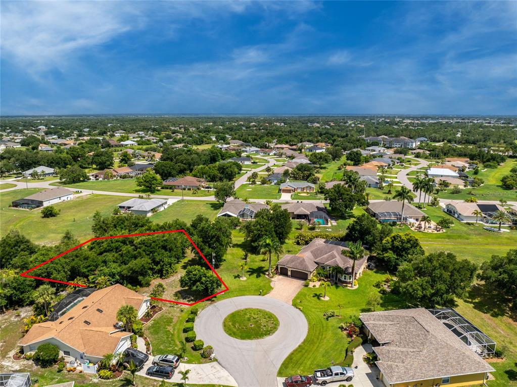 An aerial view shows a vacant, tree-covered residential lot outlined in red within a neighborhood — 26176 MAMORA DRIVE, PUNTA GORDA, FL