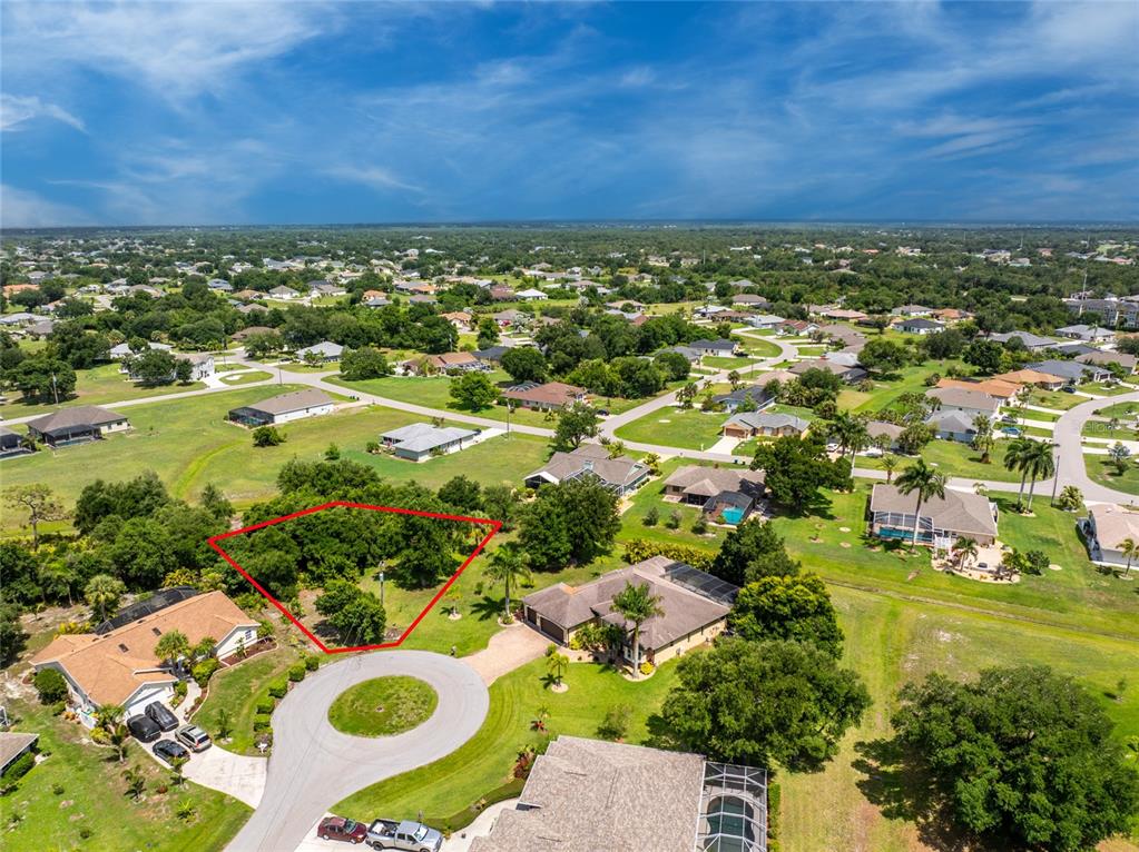 An aerial view shows a vacant, tree-covered lot outlined in red within a residential neighborhood — 26176 MAMORA DRIVE, PUNTA GORDA, FL