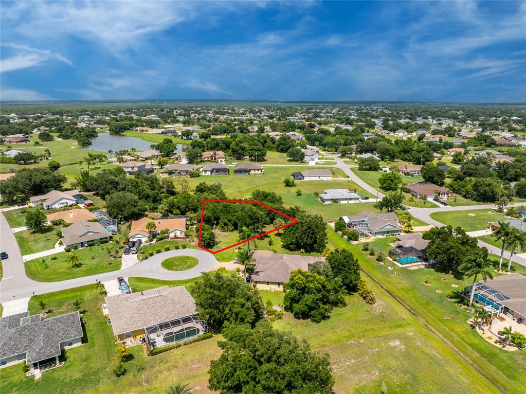 An aerial view shows a vacant, tree-covered residential lot outlined in red within a neighborhood — 26176 MAMORA DRIVE, PUNTA GORDA, FL
