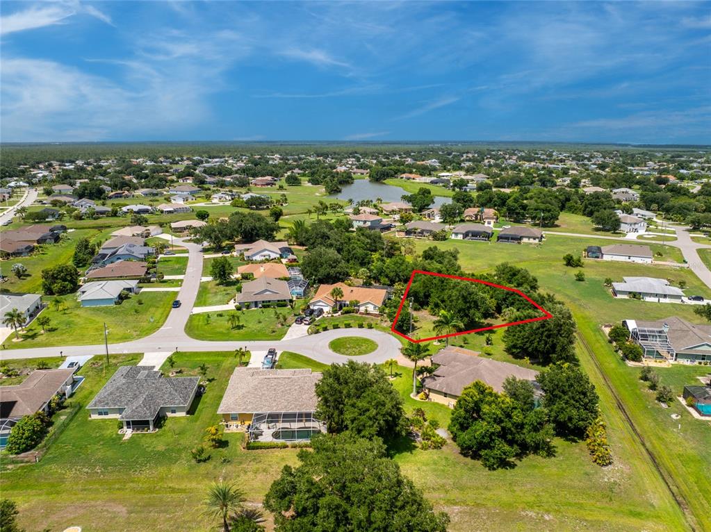 An aerial view shows a vacant, tree-covered lot outlined in red within a residential neighborhood — 26176 MAMORA DRIVE, PUNTA GORDA, FL
