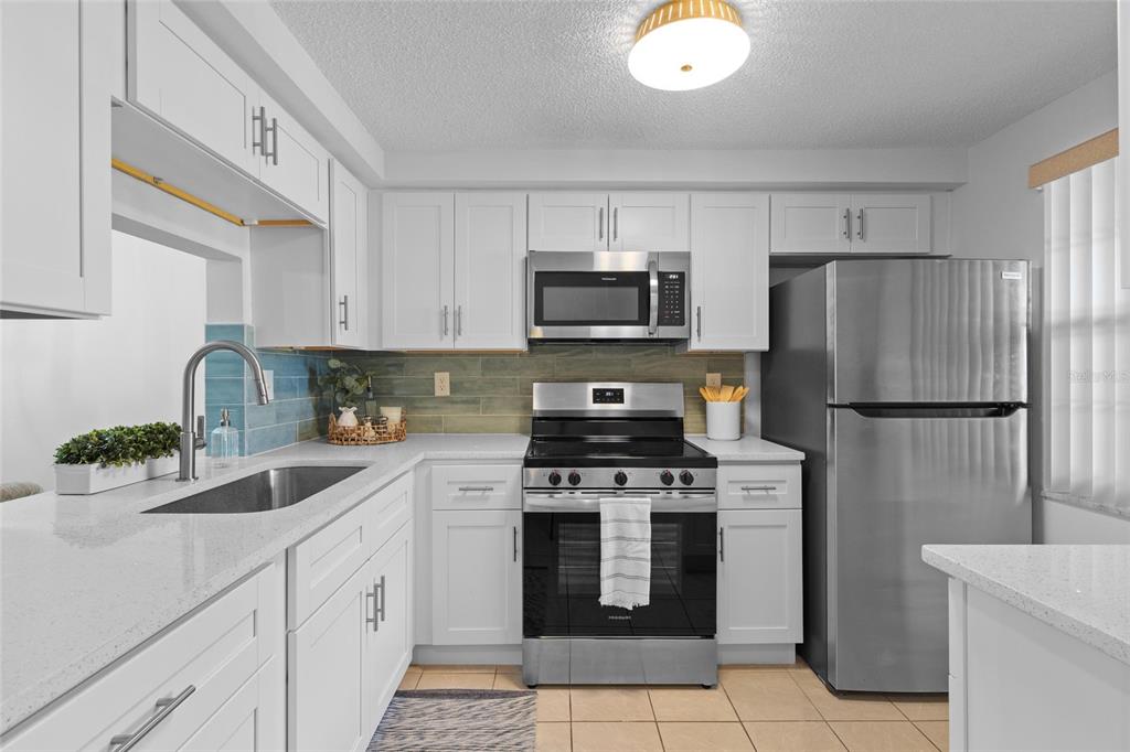 A kitchen features white cabinets, stainless steel appliances, a tiled backsplash, and light countertops — 4409 SUMMERSUN DRIVE, NEW PORT RICHEY, FL