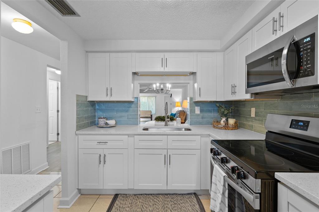 A kitchen features white cabinets, a blue tile backsplash, stainless steel appliances, and a pass-through window — 4409 SUMMERSUN DRIVE, NEW PORT RICHEY, FL