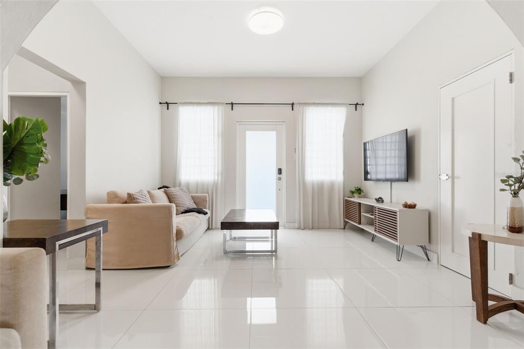 A bright living room features white tile floors, a beige sofa, and a wall-mounted television — 56 CALLE F KRUG CONDADO UNIT 5, SAN JUAN, PR