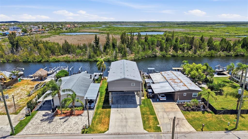 An aerial view shows three waterfront houses with boat docks along a canal and marshland — 6310 TOWER DRIVE, HUDSON, FL