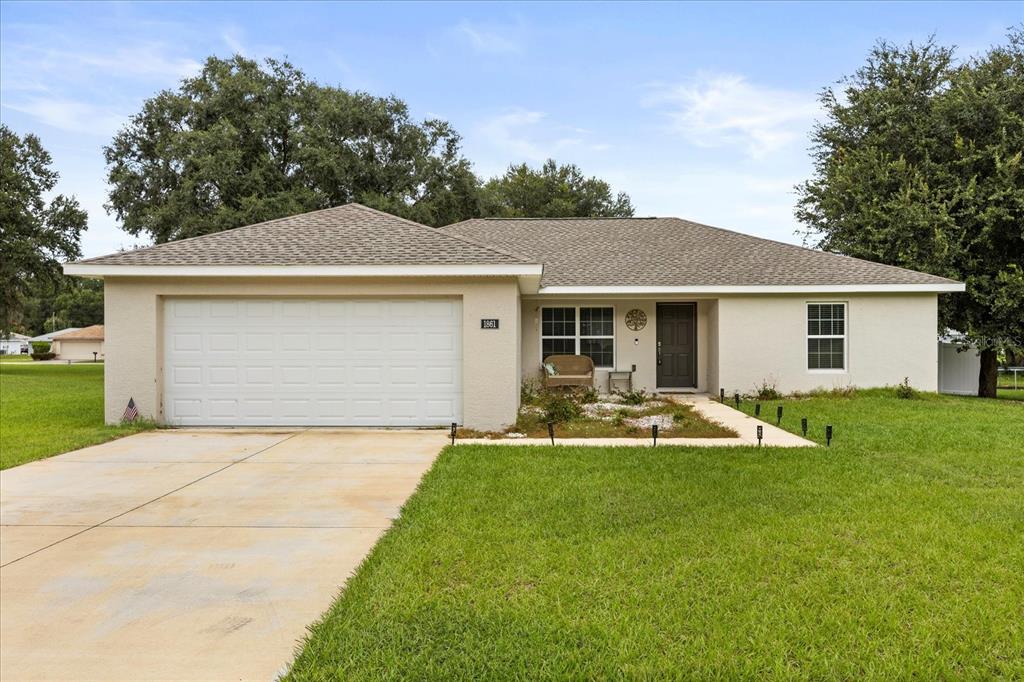 A single-story house with a beige stucco exterior, a two-car garage, and a front lawn — 1861 NE 160TH PLACE, CITRA, FL