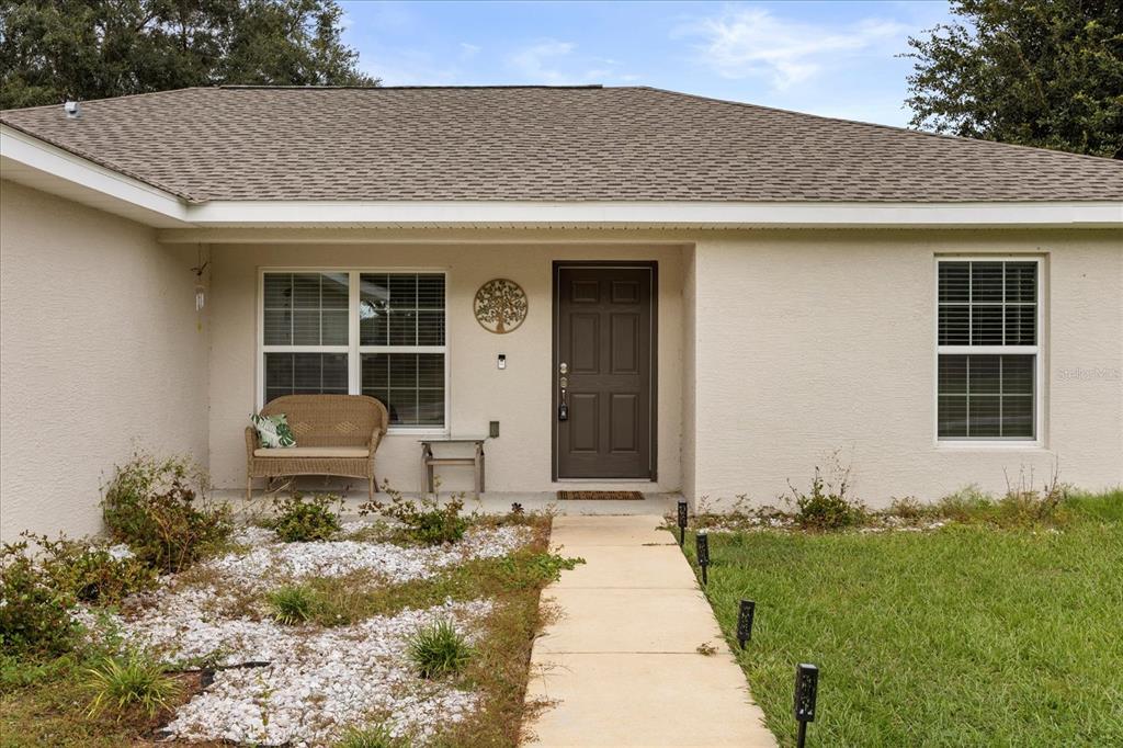 A single-story house with a beige stucco exterior, a brown front door, and a concrete walkway — 1861 NE 160TH PLACE, CITRA, FL