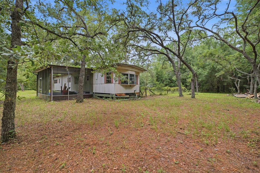 A weathered mobile home with a screened-in porch sits on a wooded, grassy lot — 1821 N SHIREY POINT, INVERNESS, FL