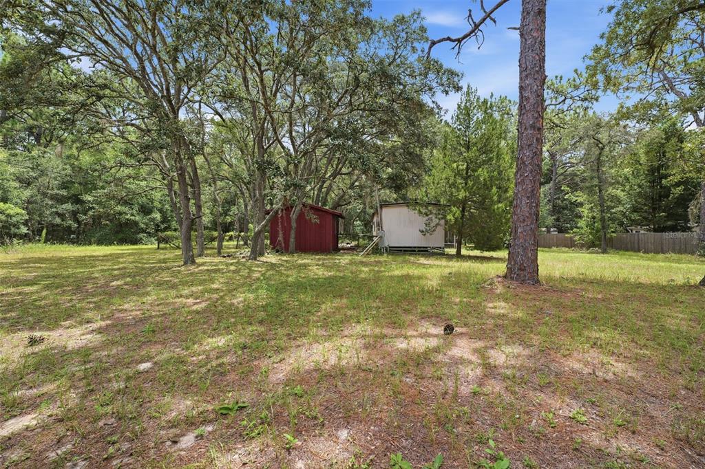 A red shed and a small mobile home sit in a grassy, tree-filled yard — 1821 N SHIREY POINT, INVERNESS, FL