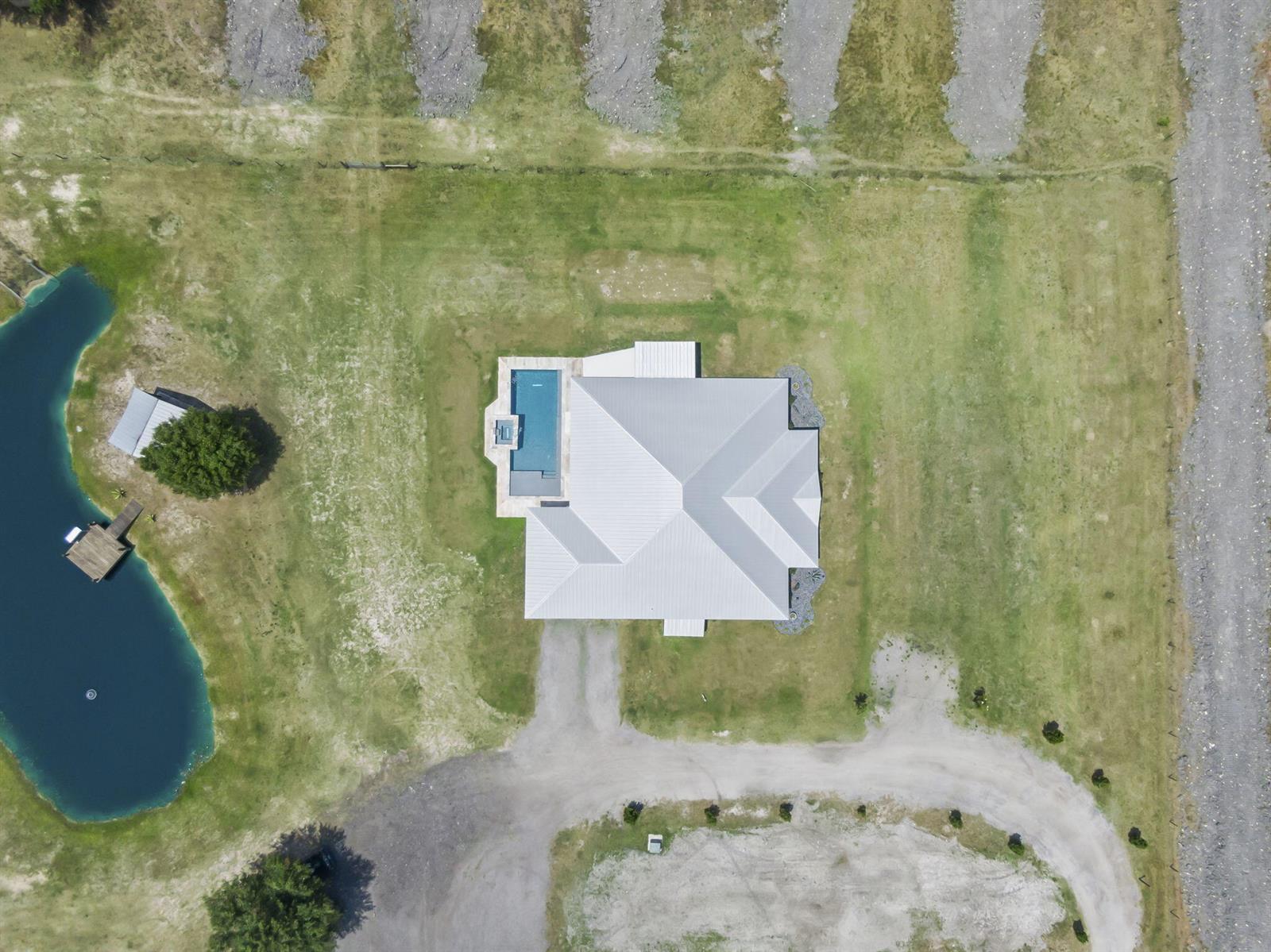 An aerial view shows a house with a metal roof and pool beside a pond — 1545 Pulitzer Road, Fort Pierce FL 34945, FORT PIERCE, FL