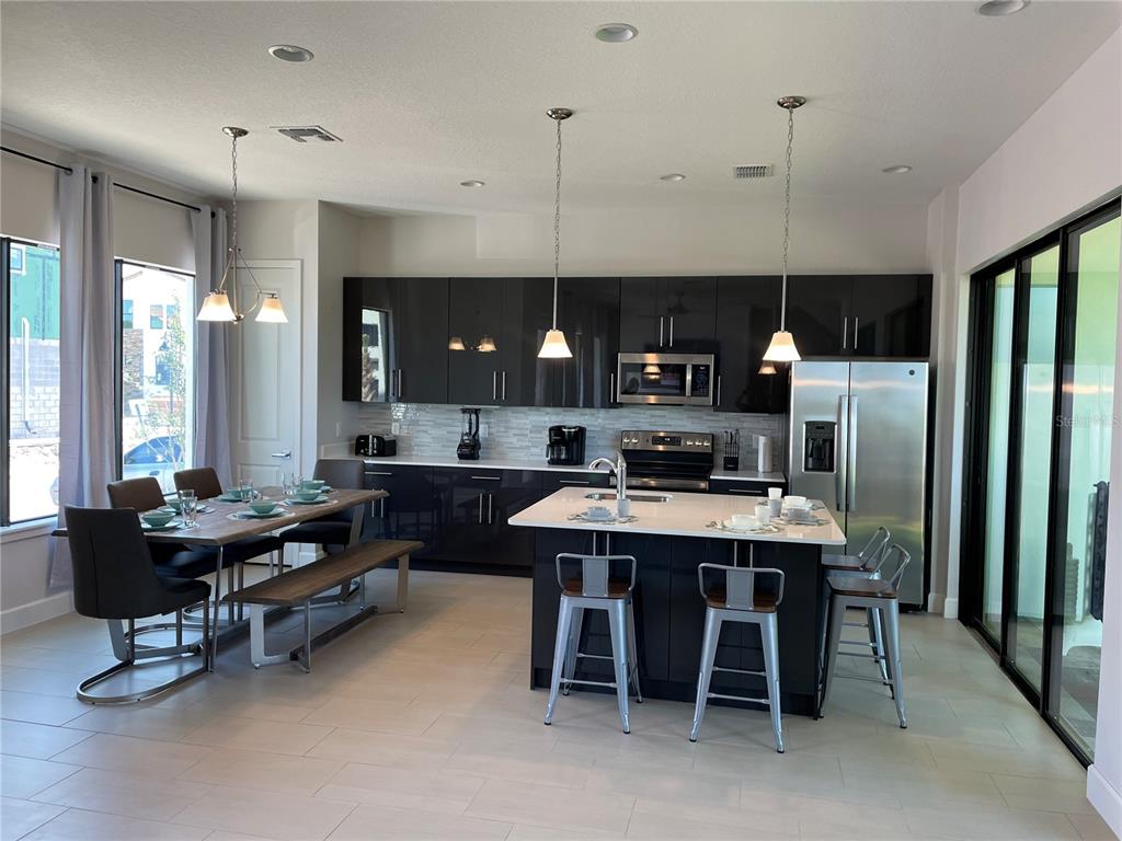 A modern kitchen features dark glossy cabinets, a white island with bar stools, and dining area — 108 VILLA DOMANI CIRCLE, DAVENPORT, FL