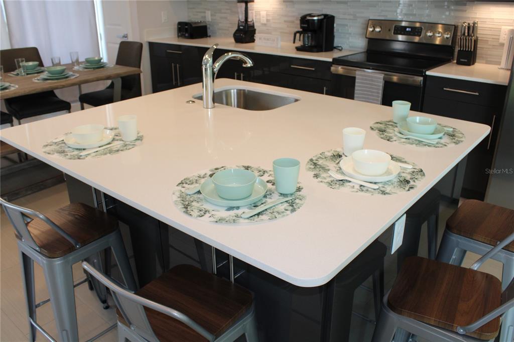 A modern kitchen features a large white quartz island with seating and a stainless sink — 108 VILLA DOMANI CIRCLE, DAVENPORT, FL