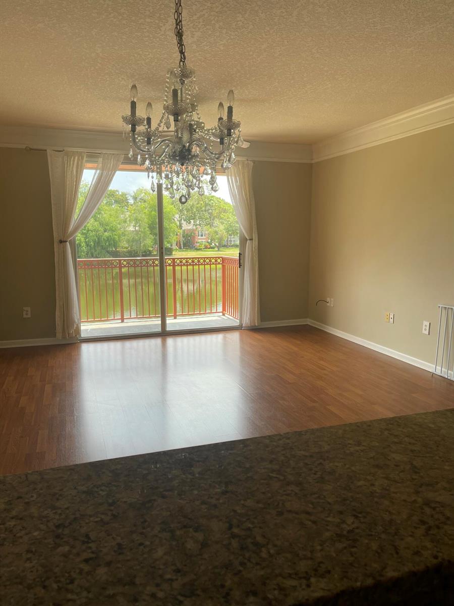 An empty living room features wood-look flooring, a crystal chandelier, and a sliding glass door — 2040 Alta Meadows Lane # 1605, Delray Beach FL 33444, DELRAY BEACH, FL