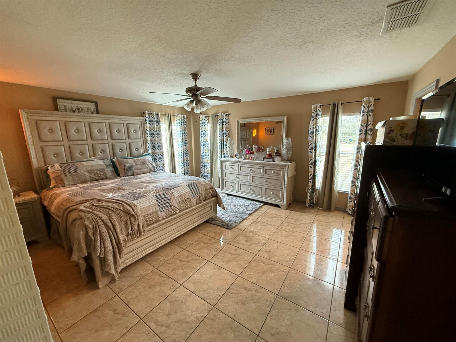 A bedroom with a large tufted headboard, tiled floors, a ceiling fan, and a dresser — 4010 Watkins Road, FL 33844, FL