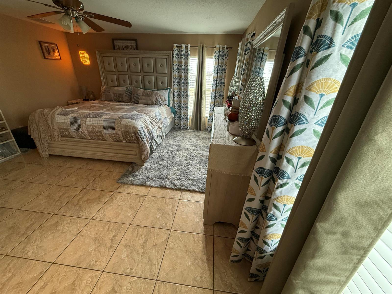 A bedroom features a tufted headboard, tile flooring, a gray area rug, and patterned curtains — 4010 Watkins Road, FL 33844, FL