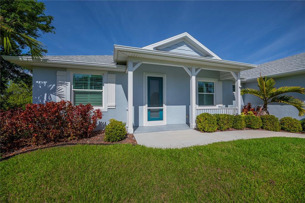 A light blue house exterior features a covered front porch, white trim, and landscaped lawn — 9453 SINGER CIRCLE, PORT CHARLOTTE, FL