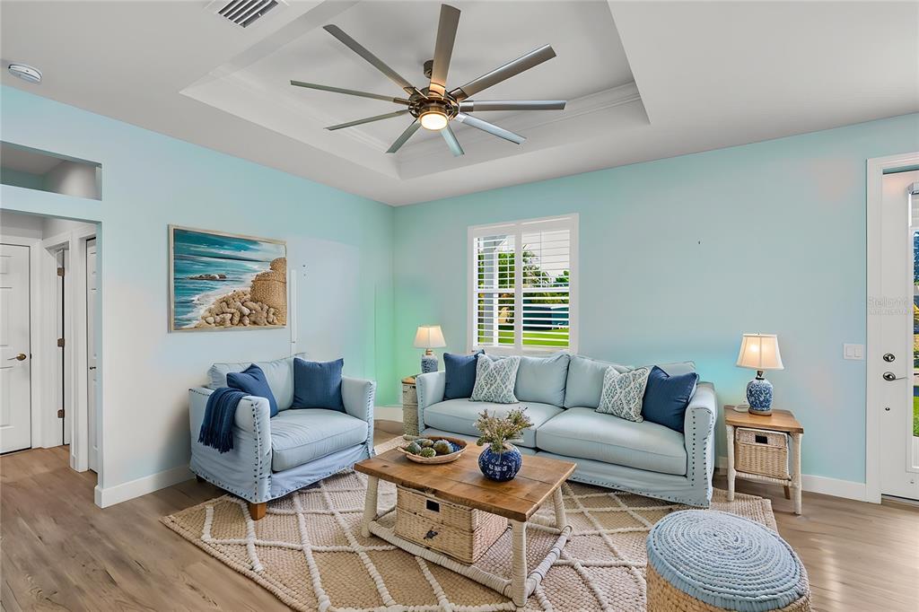 A living room features light blue walls, a tray ceiling with a fan, and coastal furniture — 9453 SINGER CIRCLE, PORT CHARLOTTE, FL