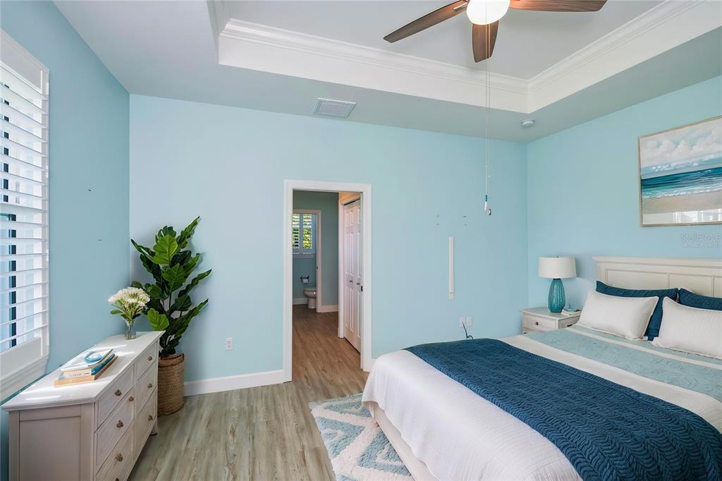 A bedroom features light blue walls, a tray ceiling with a fan, and wood-look flooring — 9453 SINGER CIRCLE, PORT CHARLOTTE, FL
