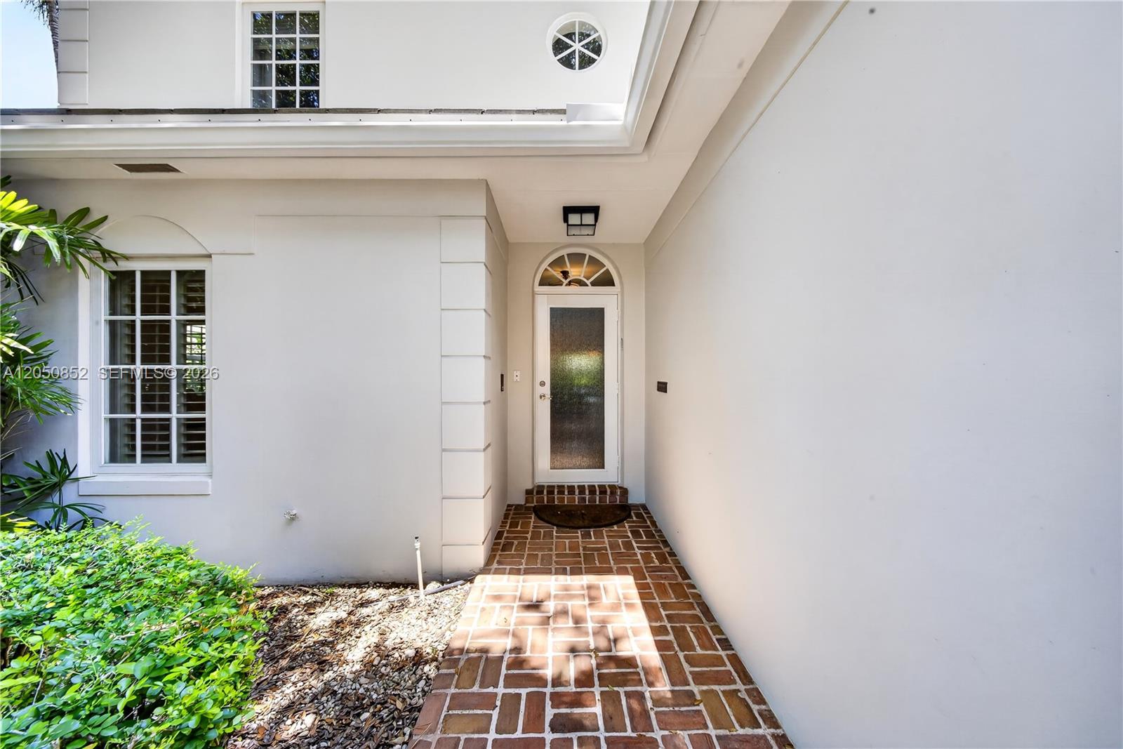 A white exterior home entrance features a brick walkway and a glass-paneled front door — 4820 Campo Sano Ct, Coral Gables FL 33146, CORAL GABLES, FL