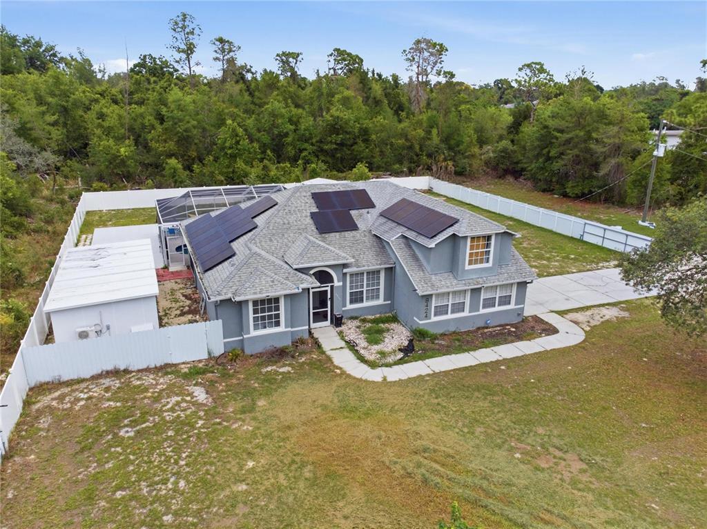 An aerial view shows a gray house with solar panels and a fenced backyard — 8424 BALM STREET, WEEKI WACHEE, FL