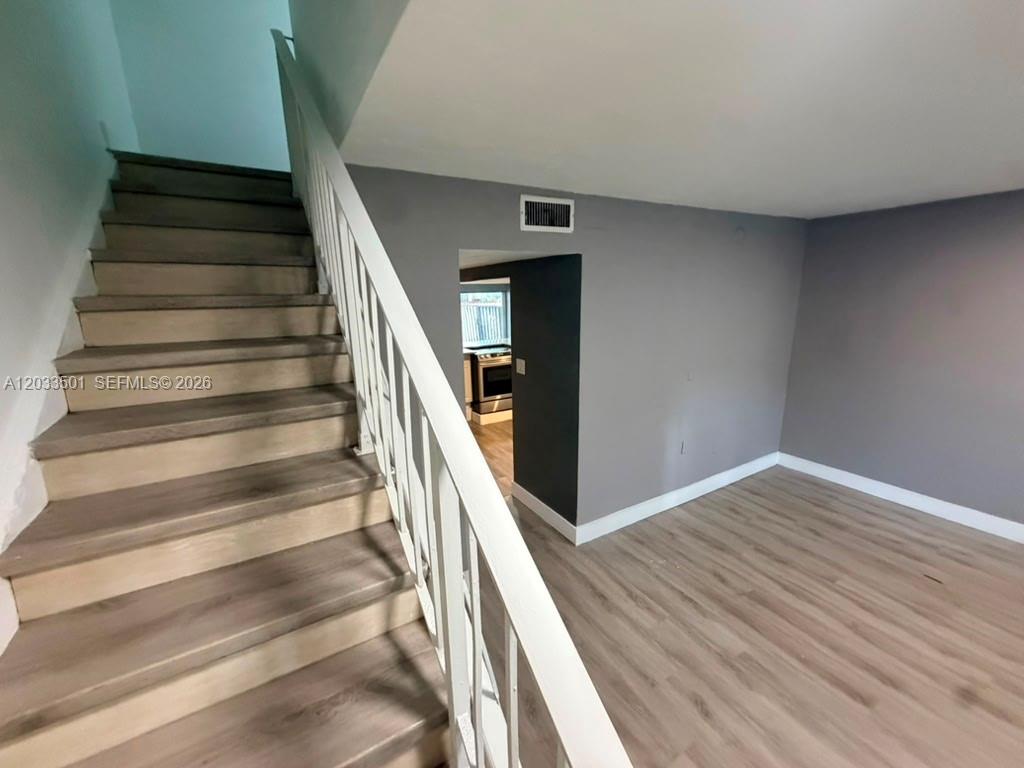 A staircase with light wood steps and a white railing leads to an upper level — 274 NE 141st St # 3C, Miami FL 33161, MIAMI, FL