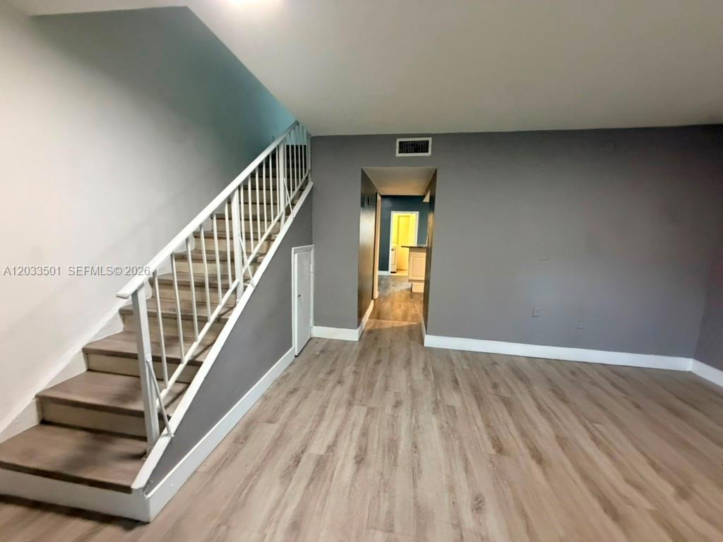 A room with wood-look flooring, a white staircase, and a doorway leading to another area — 274 NE 141st St # 3C, Miami FL 33161, MIAMI, FL
