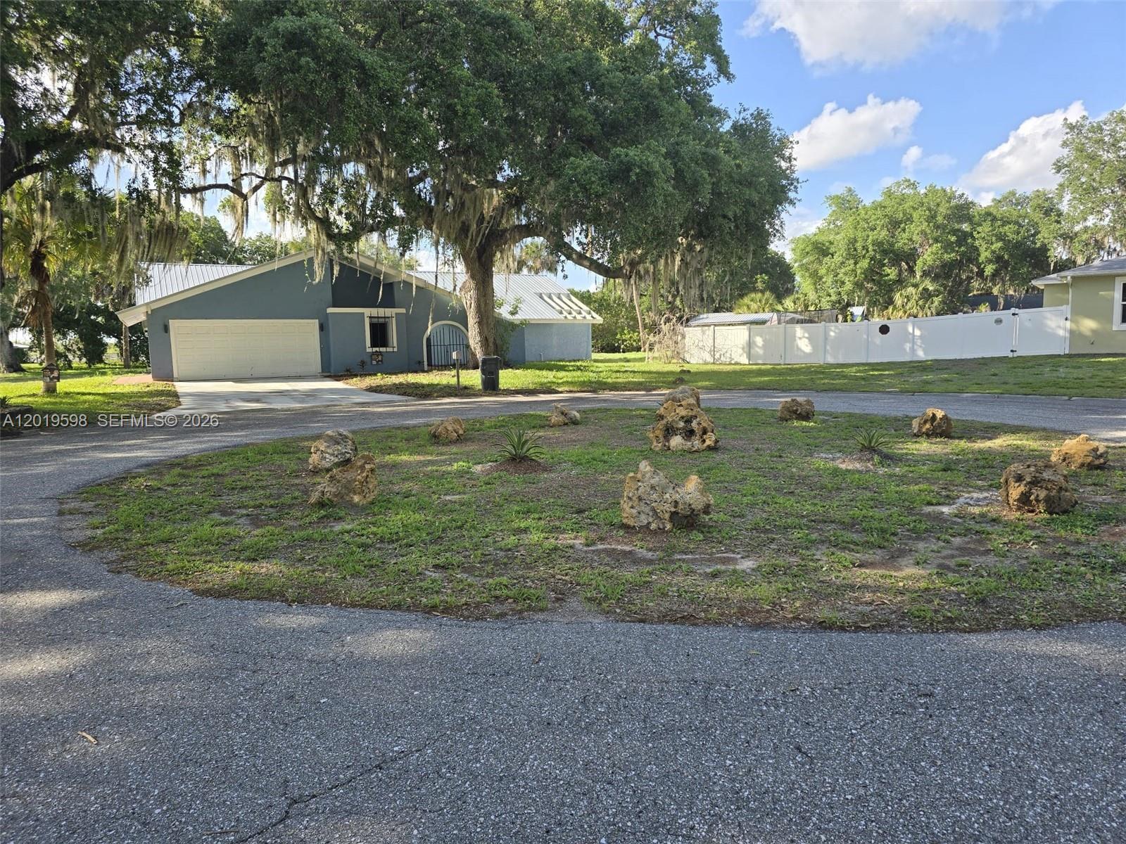 A circular garden bed with scattered rocks sits in front of a blue house — LA BELLE, FL