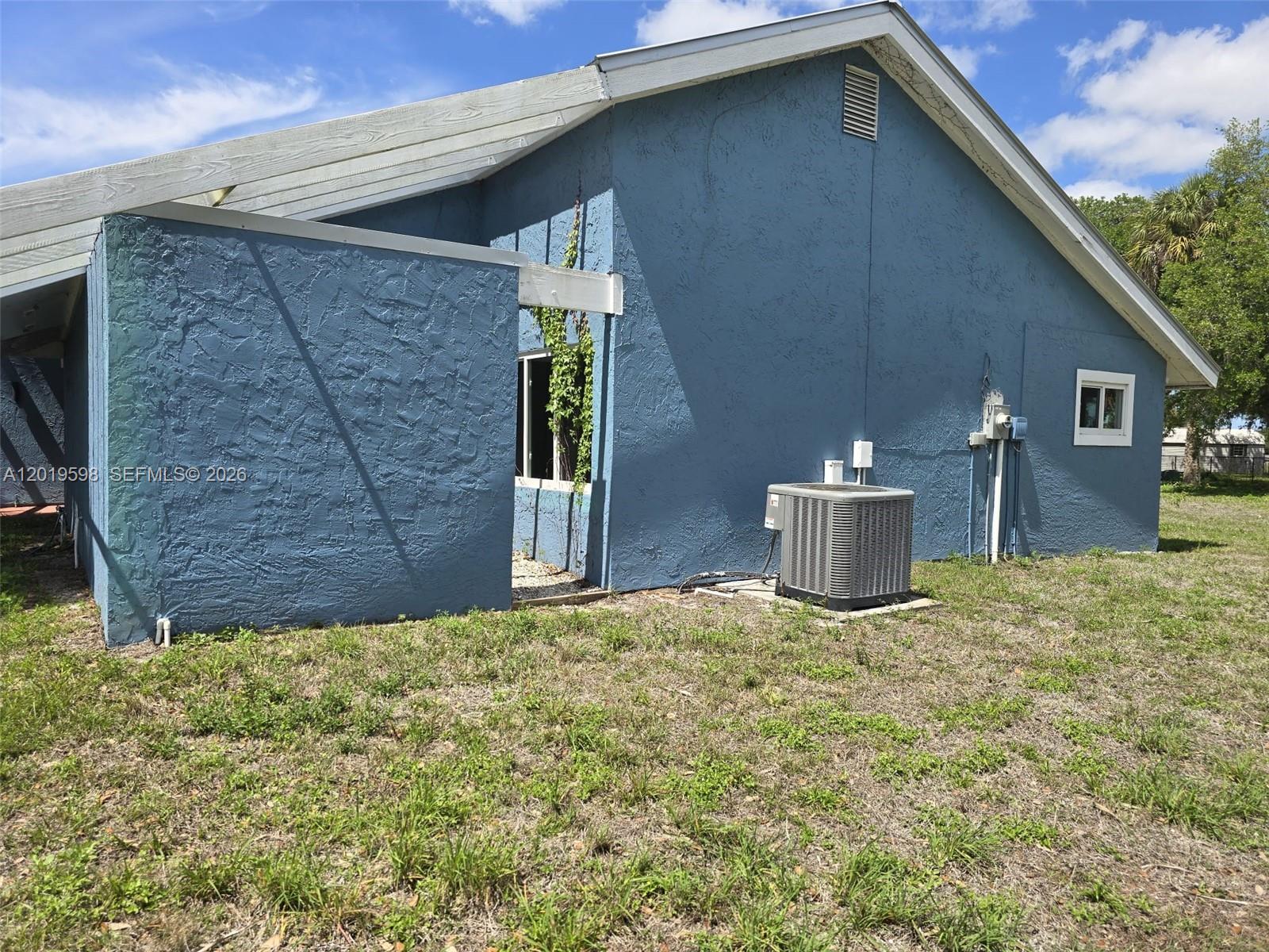 The exterior of a blue stucco house features an HVAC unit and a small window — LA BELLE, FL