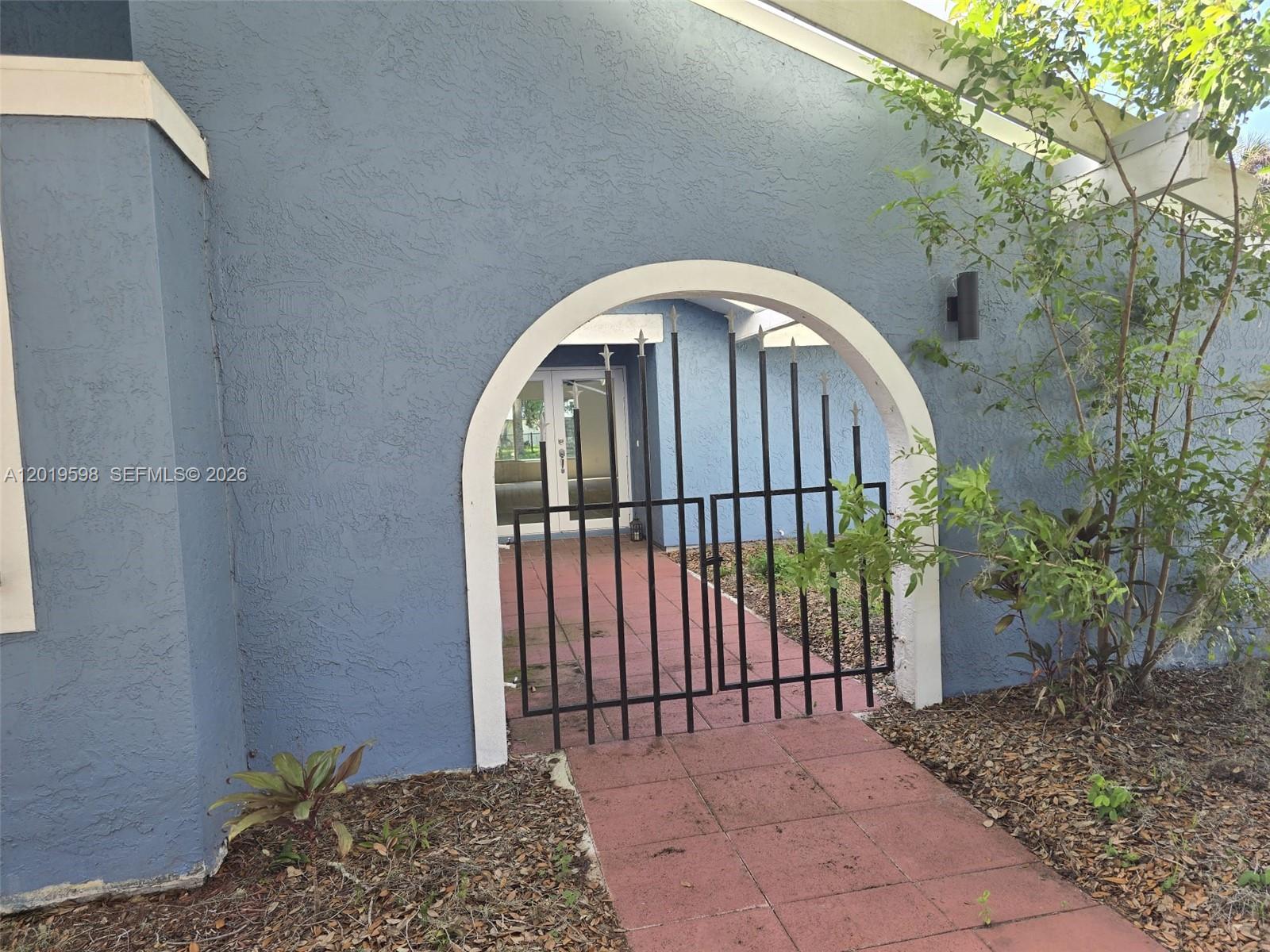 A blue exterior wall features an arched entryway with a black metal gate — LA BELLE, FL