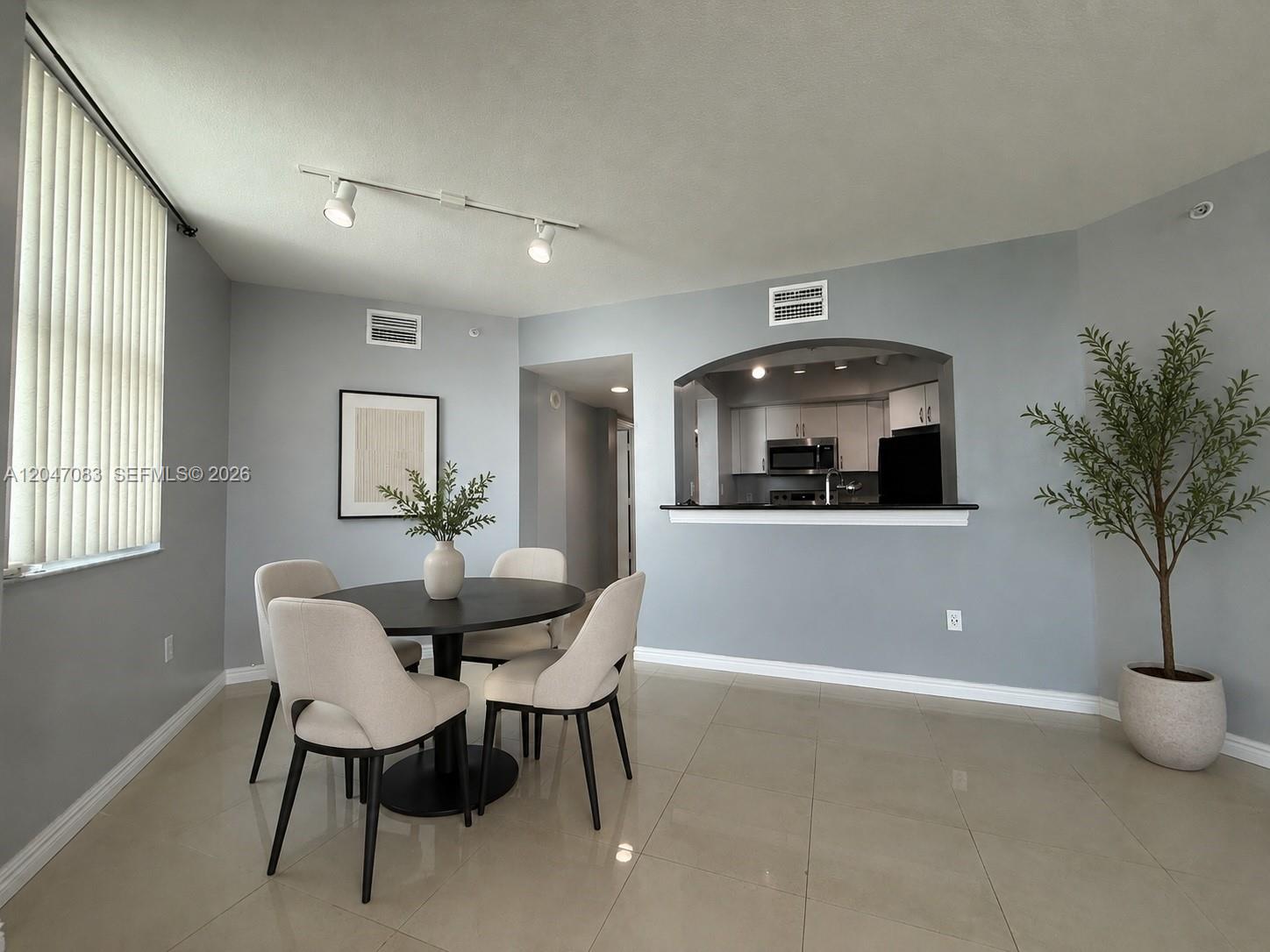 A dining area with a round table, four chairs, and an arched kitchen pass-through window — 9201 Collins Ave # 521, Surfside FL 33154, SURFSIDE, FL