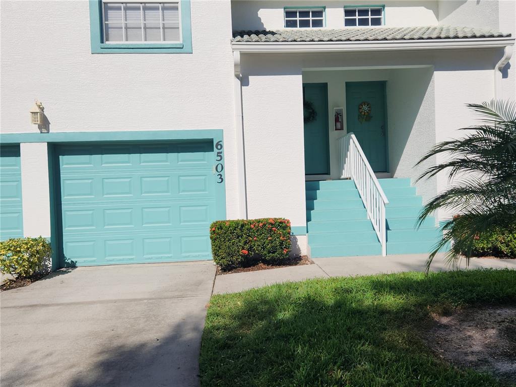 A two-story townhouse exterior features a teal garage door, matching stairs, and white stucco walls — 6503 FAIRWAY GARDENS DRIVE, BRADENTON, FL