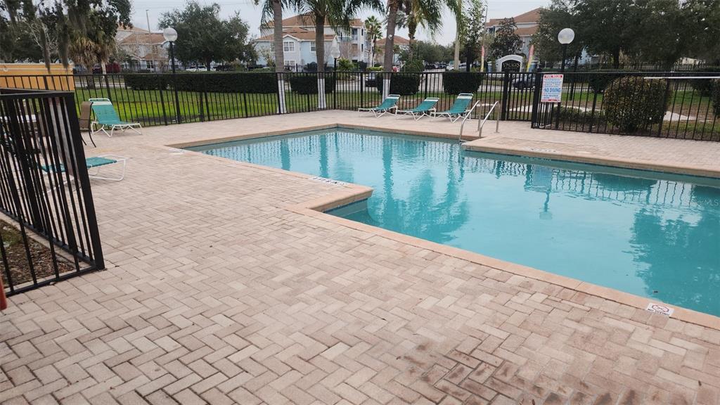 A rectangular swimming pool with a paver deck is enclosed by a black metal fence — 4540 COMMANDER DRIVE UNIT 2224, ORLANDO, FL